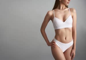 Woman with a skinny physique stands and poses while wearing white panties and bra.